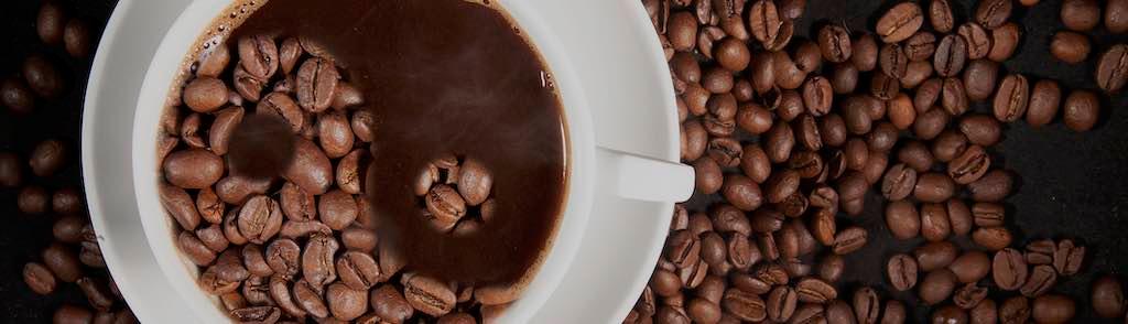 Cup of aromatic coffee with coffee beans on a dark background