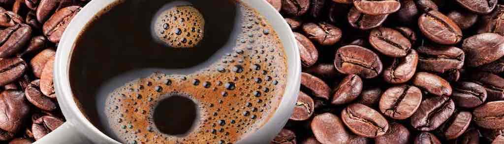 Cup of coffee americano over roasted coffee beans. Symbol yin and yang formed of foam.