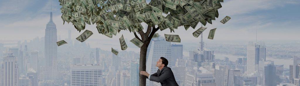 A businessman grabs the trunk of a money tree with both hand as he tiries to shake loose the money that is growing on it.  The tree is growing in a parkway and the New York City skyline can be seen in the distance.